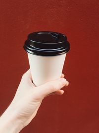 Cropped hand of woman holding disposable cup against brown background