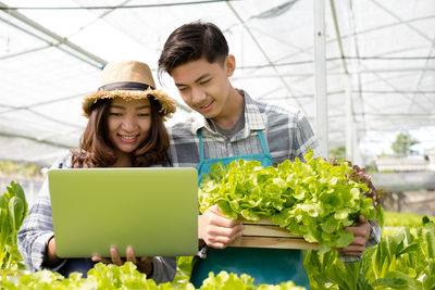 Smiling botanist looking at laptop while holding vegetable at greenhouse