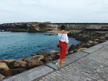 Rear view of woman walking on pier by sea against sky