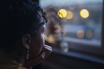 Pensive young woman looking through window