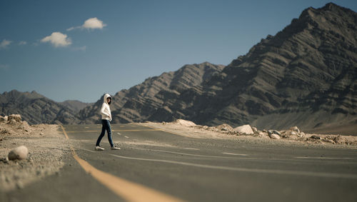 Woman walking on road by mountains against sky