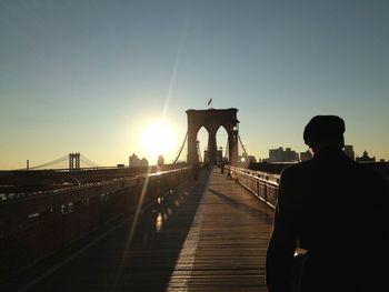 Rear view of man walking on brooklyn bridge against sky during sunset