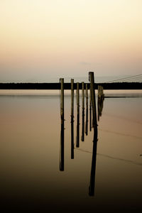 Wooden posts in lake against sky during sunset