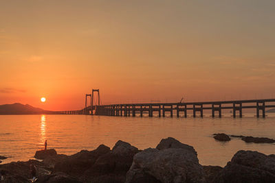 Silhouette bridge over sea against sky during sunset