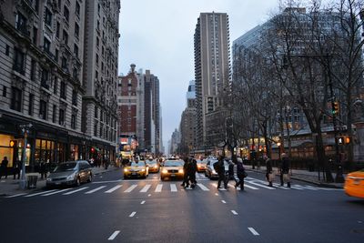 Cars and people on road amidst buildings at dusk