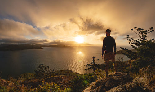 Man standing on rock against sky during sunset