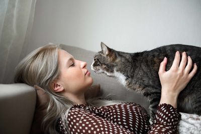 A young woman talking to a cat at home on the couch 