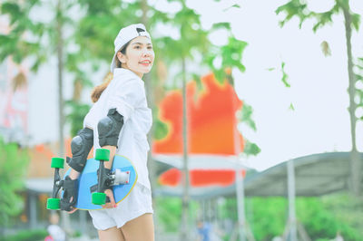 Woman holding skateboard while standing outdoors