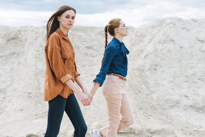 Full length of sisters models walking on beach
