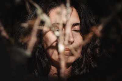 Portrait of a woman catching sun with closed eyes between branches in the forest