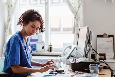 Side view of female nurse making medical report in computer at clinic