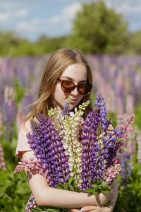 Young woman in the field of flowers with bunch of lupines