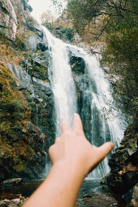 Cropped image of person hand against waterfall