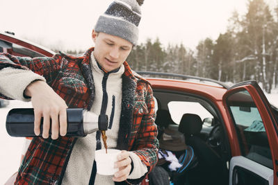 Mid adult man pouring coffee from insulated drink container while standing by car