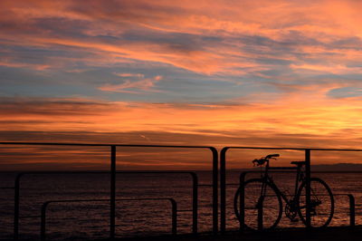 Bicycle by sea against sky during sunset