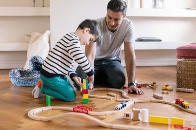 Smiling father playing with son while kneeling in living room