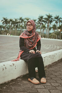 Thoughtful young woman sitting on dividing line at street
