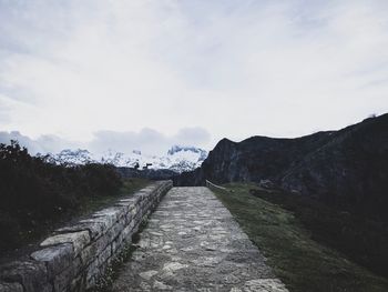 Empty road leading towards mountains against sky