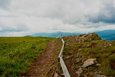 Dirt road amidst land against sky