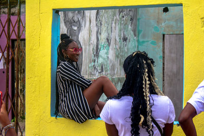 Side view of woman wearing sunglasses sitting on window sill