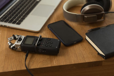 From above of audio recorder and headphones placed on wooden table with laptop and notebook for recording podcast at home