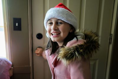 Smiling girl in santa hat standing at home