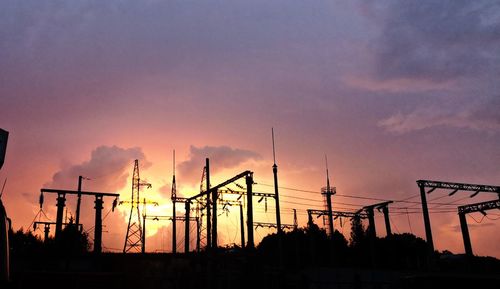 Silhouette cranes at construction site against sky during sunset