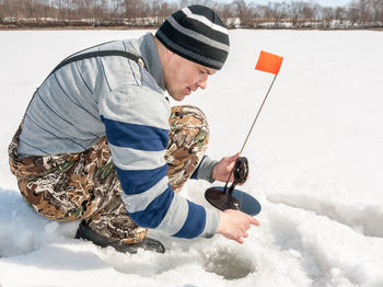 Side view of mid adult man subglacial fishing in frozen lake