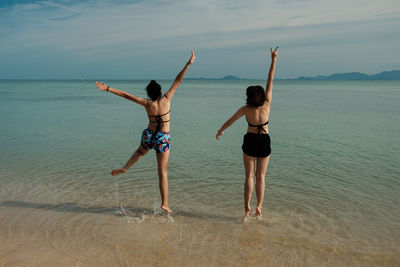 Rear view of friends jumping on shore at beach