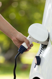 Cropped image of hand charging electric white car at park