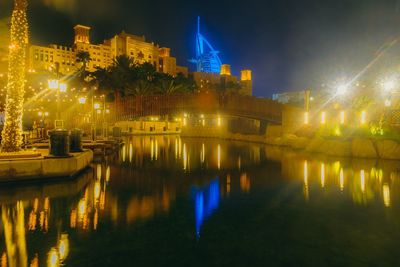 Illuminated buildings in front of canal against sky at night