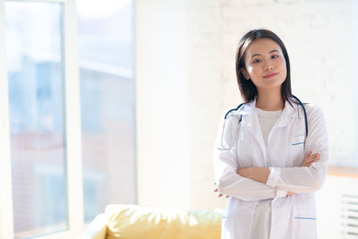Portrait of female doctor standing against window