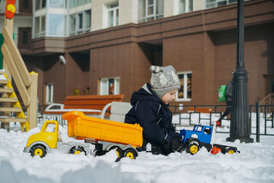 Cute little caucasian boy playing with big toy plastic truck at playground on winter