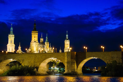 Arch bridge over river amidst buildings at dusk