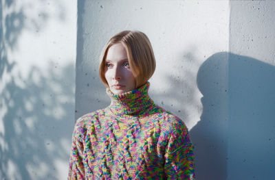 Blond woman in a sweater standing near a concrete wall in the forest.