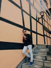 Full length of fashionable man standing on steps against wall