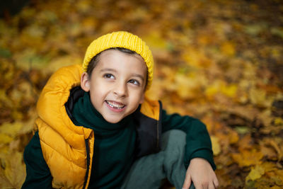 Portrait of a fashionable child boy autumn sitting on a trail in orange leaves in the afternoon