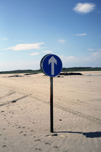 Road sign on beach against blue sky