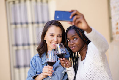 Smiling friends holding wineglass taking selfie at cafe