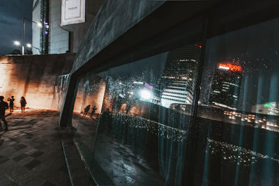 People walking on illuminated street amidst buildings at night