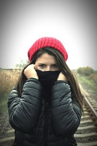 Portrait of young woman wearing warm clothing standing against sky during winter