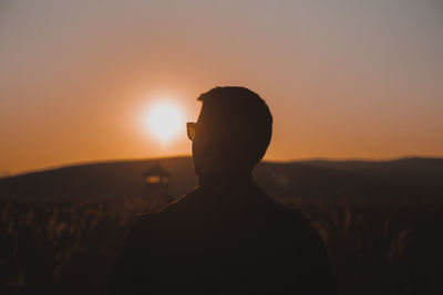 Young man from behind wearing glasses at sunset