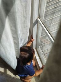 High angle view of boy crouching by window at home