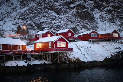 House by frozen lake by houses against snowcapped mountains during winter
