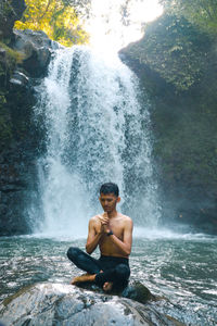 Full length of shirtless man splashing water in rocks