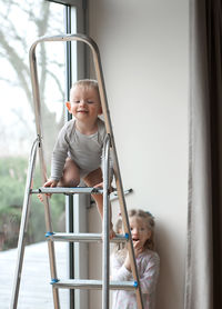 Baby boy by sister on ladder at home