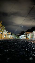 Illuminated street by buildings against sky at dusk