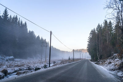 Street amidst trees against clear sky during winter