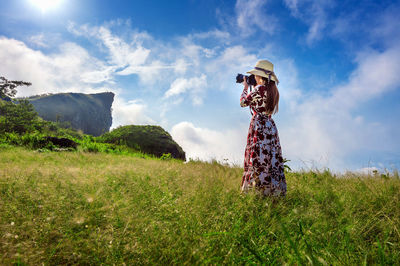 Side view of woman photographing while standing on grassy field