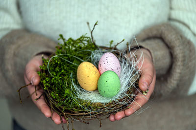 Nest with an colorful easter eggs in female hands, easter decor in rustic style